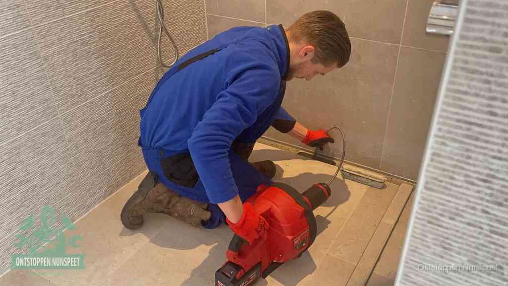 Een monteur ontstopt een langwerpige douchegoot met een elektrische veer, een doucheputje verstopt door haren en zeep in Nunspeet