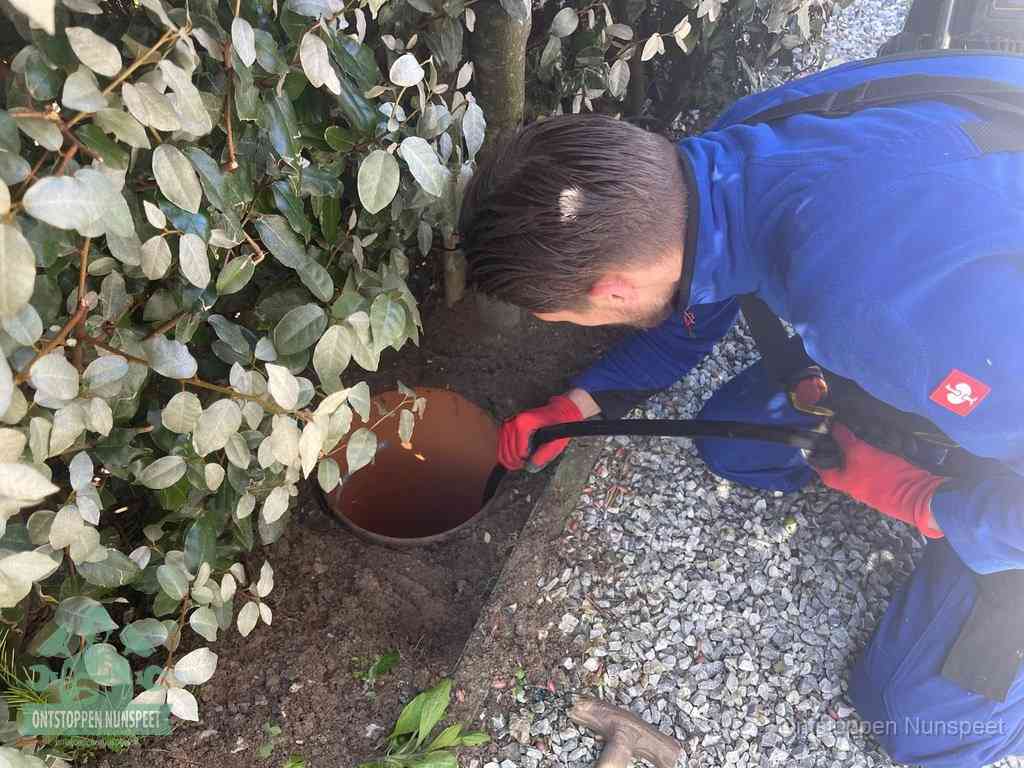 Een monteur voert een slang in een geopende rioolput in de tuin om het hoofdriool te ontstoppen in Nunspeet